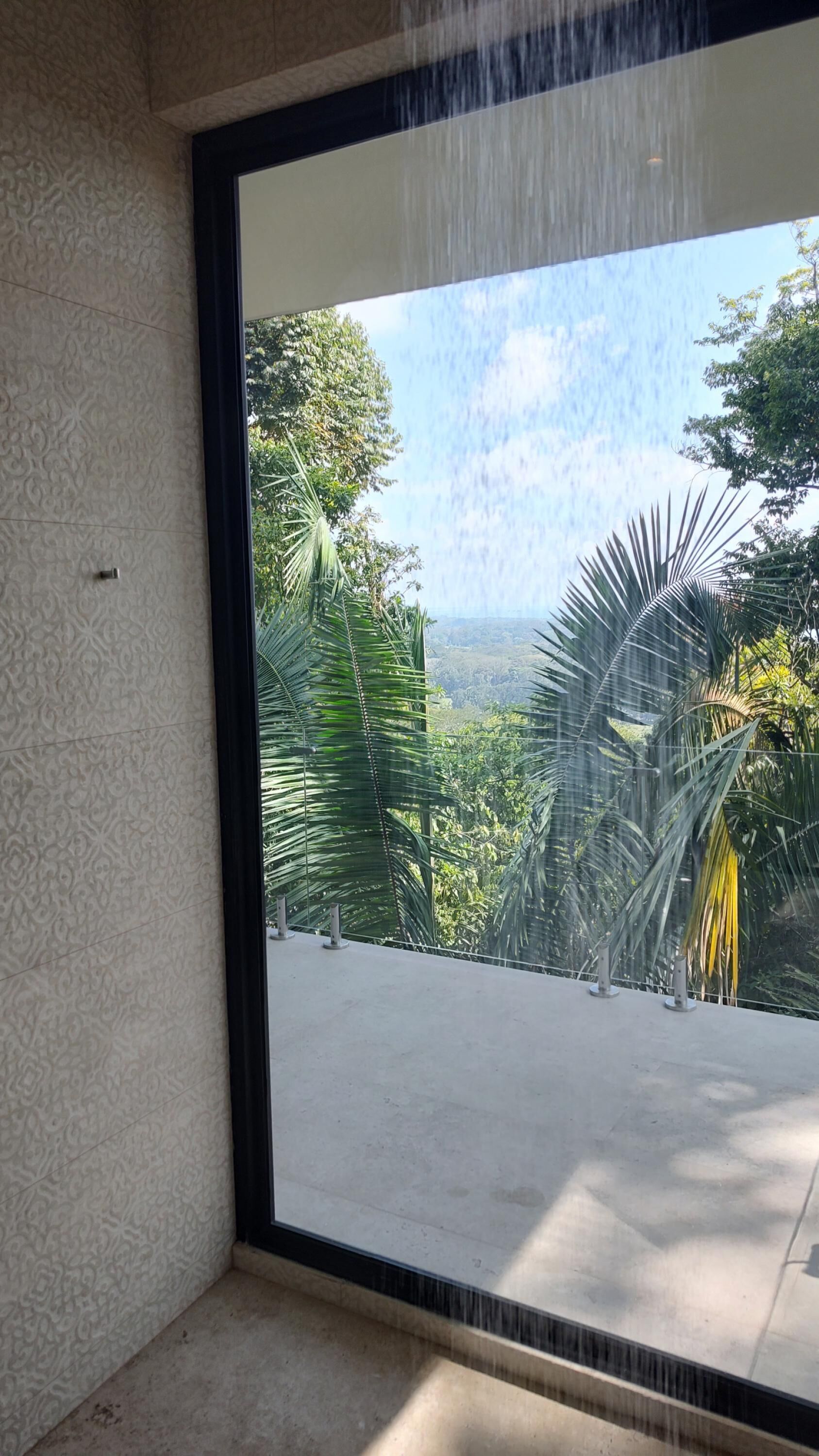 Una habitación con un gran ventanal corredera que da a un balcón con vistas a exuberante vegetación y un paisaje lejano.