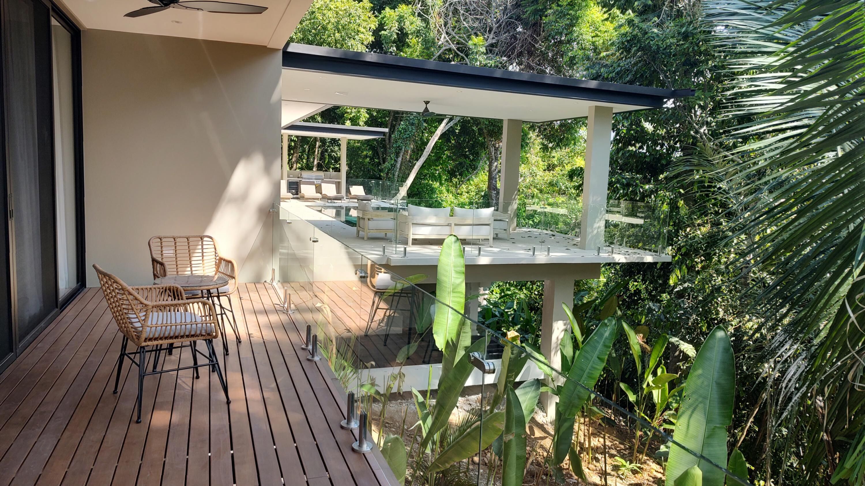 A wooden deck with wicker chairs, a glass balustrade, and a white outdoor seating area with cushions.