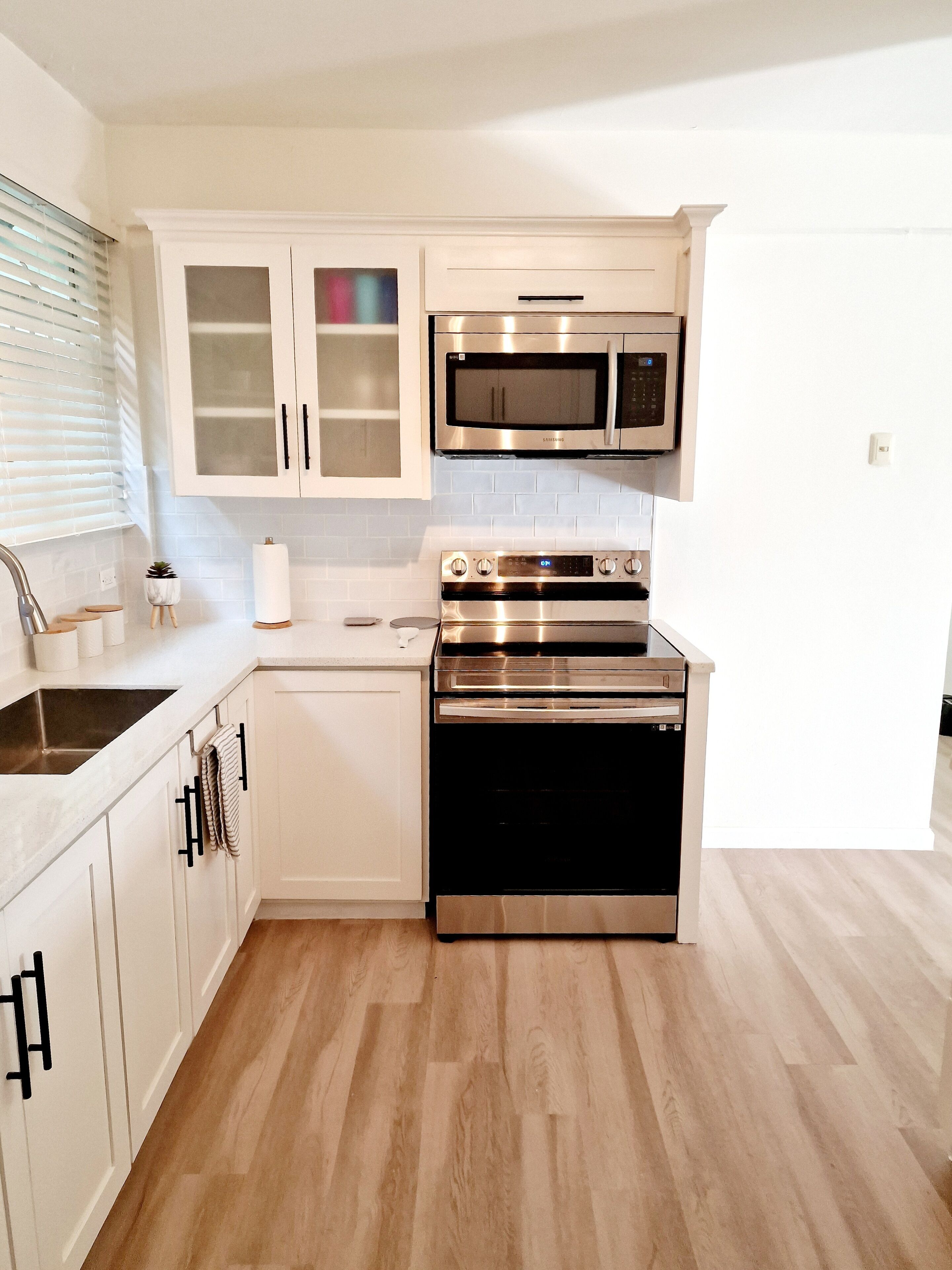 Une cuisine moderne avec des armoires blanches, des appareils en acier inoxydable et un plancher en bois.