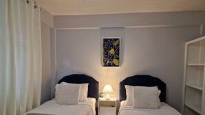 Une chambre double avec deux lits, une table de chevet avec une lampe, un tableau au mur et une bibliothèque.