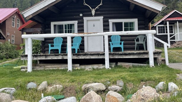 Una baita di legno con un portico, due poltrone Adirondack color turchese e un teschio di cervo appeso sopra l'ingresso.