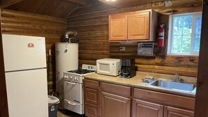 Una cucina compatta con pareti in legno, un frigorifero, fornello, microonde, macchina del caffè e lavandino.