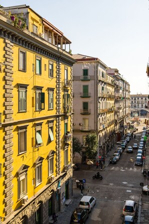 A street view with yellow buildings, parked cars, and a cobblestone road. - The Place :: Designer Apartment Near the Main Train Station (Napoli)