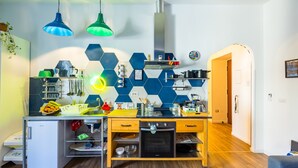 Una cocina compacta con refrigerador integrado, microondas y estufa. Hay una encimera de madera con diversos utensilios de cocina y un protector contra salpicaduras de azulejos hexagonales.