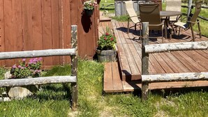 Een houten hutje met een terras, buitenmeubels en uitzicht op verre bergen.