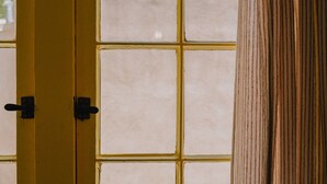 Una habitación con un ventanal grande dividido en varios paneles, una puerta de madera con marco amarillo y un pilar de madera.