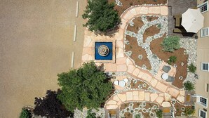 Vista aérea de un patio ajardinado con fuente circular central, senderos de piedra y zonas de estar al aire libre.