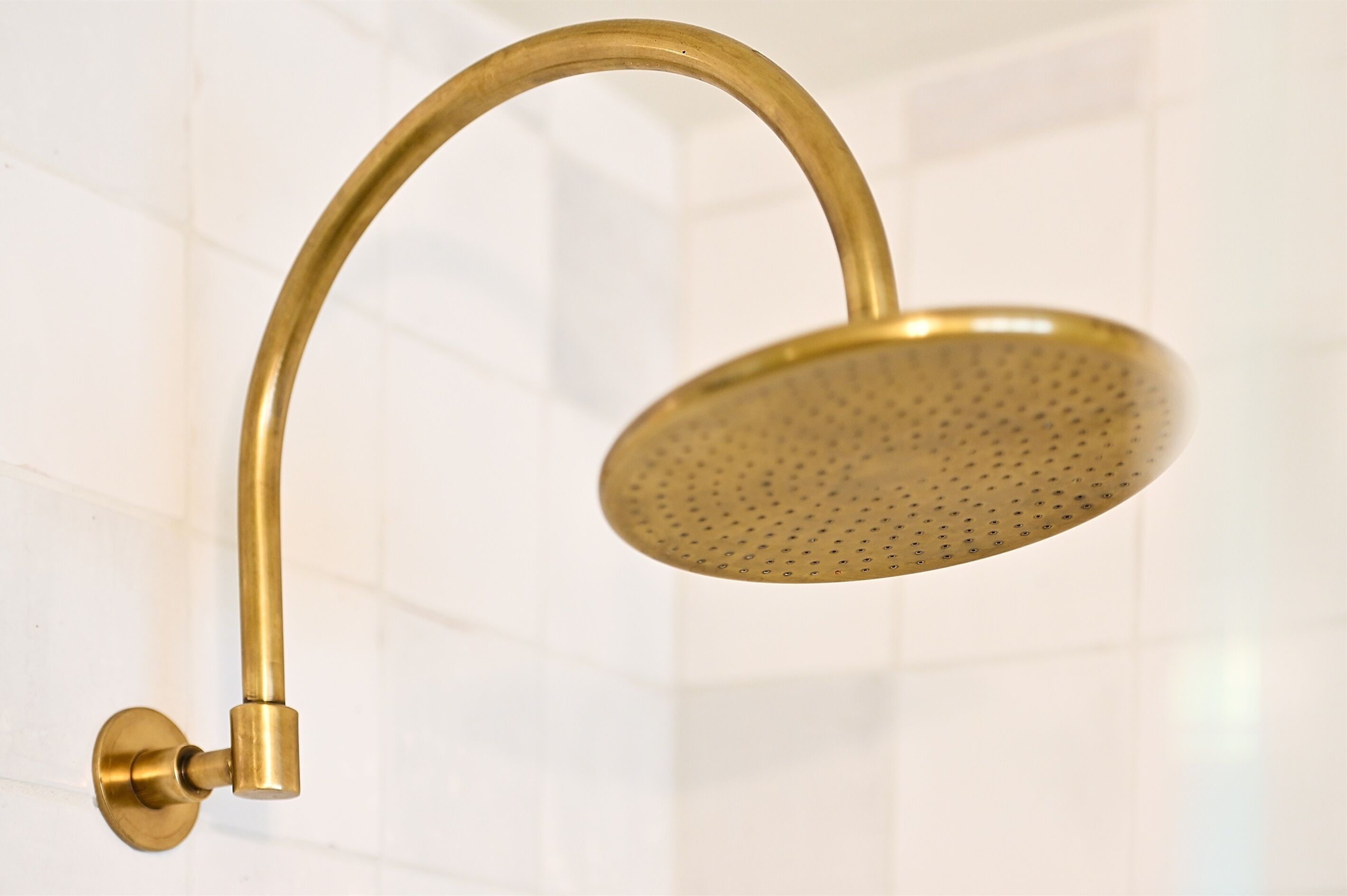 A gold-colored showerhead with a curved handle, mounted on a wall with white tiles.