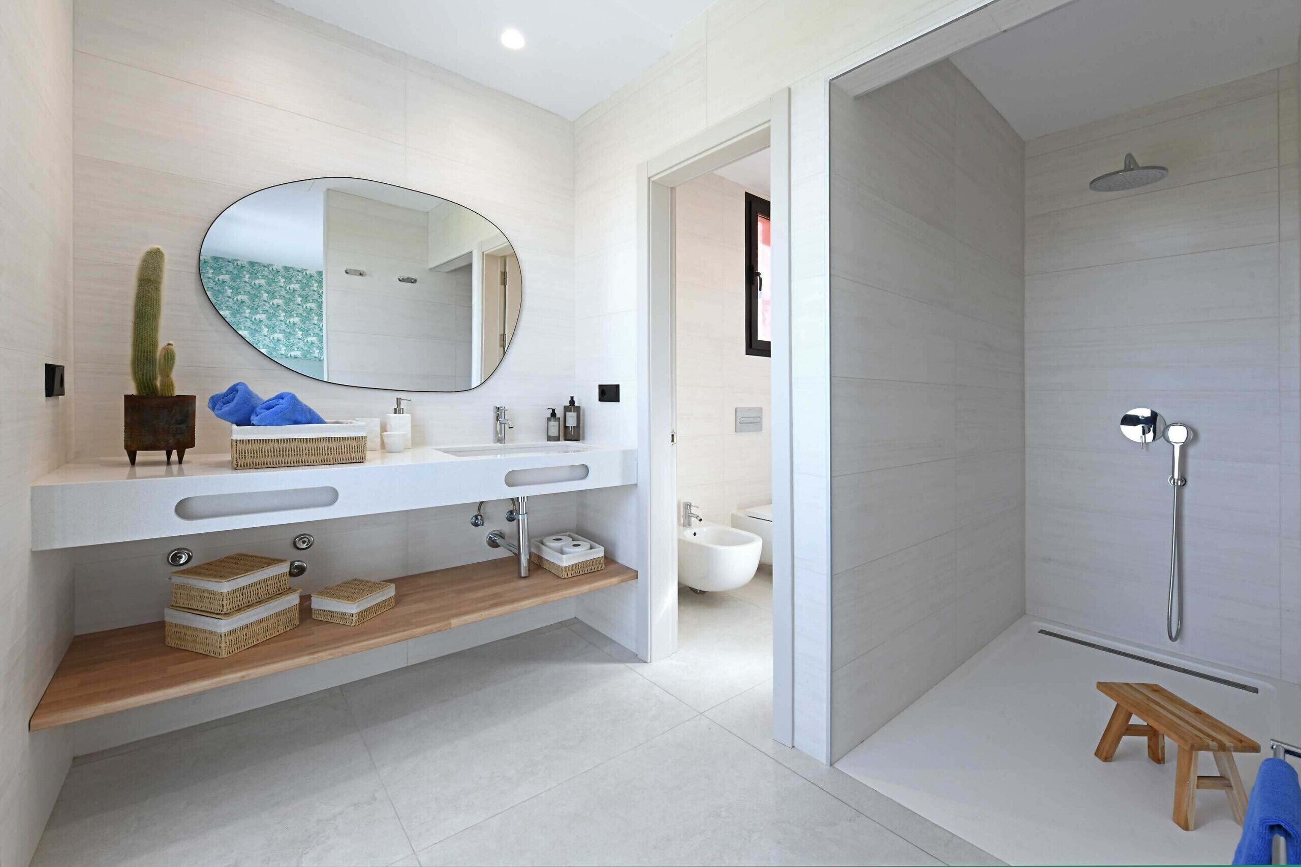 A modern bathroom with a large mirror, two sinks, a shower, and a wooden bench.