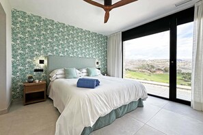 Ein Schlafzimmer mit einem großen Bett, einem Nachttisch, einem Deckenventilator und Blick auf eine Landschaft durch eine Schiebetür.