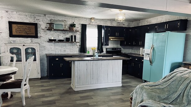 A kitchen with a central island, dark cabinets, and a light blue refrigerator. - Sunsets in Brookston (Brookston)