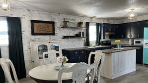 A kitchen with dark cabinets, a white island, and a dining area with white chairs. - Sunsets in Brookston (Brookston)