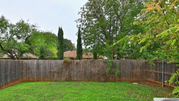 A backyard with a wooden fence, a lawn, and a tree. - Downton Abbey - A Sayles Ranch Home (Abilene)