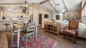 A spacious loft with a high ceiling, exposed wooden beams, a dining area with a wooden table and chairs, a cozy seating area with a sofa and armchairs, and a kitchen with modern appliances. - Charming Home in Country Club Flagstaff with Views (Flagstaff)