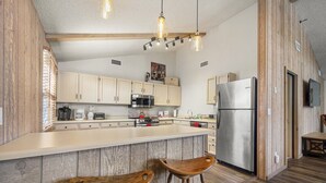 A modern kitchen with wooden accents, a large island, bar stools, and stainless steel appliances. - Charming Home in Country Club Flagstaff with Views (Flagstaff)
