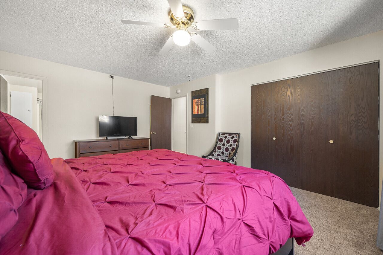 A bedroom with a large bed, a ceiling fan, a TV, a wardrobe, and a chair.