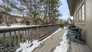 A wooden deck with snow, a railing, and two Adirondack chairs. - Charming Home in Country Club Flagstaff with Views (Flagstaff)