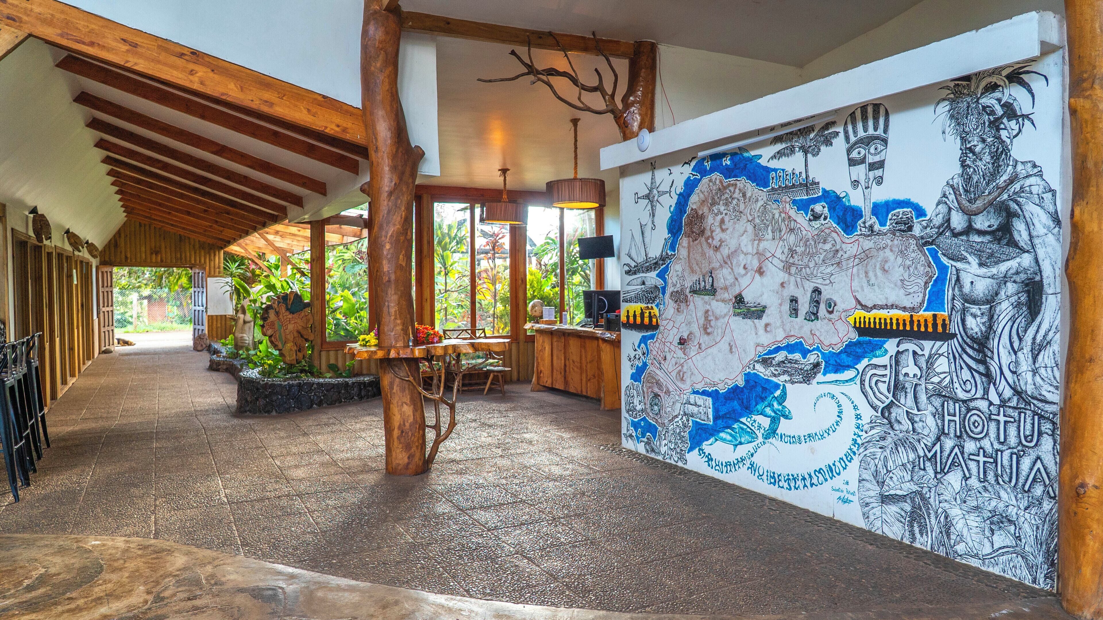 Un amplio pasillo con vigas de madera, un mural con motivos marítimos y culturales, y una zona de estar con una mesa y sillas.