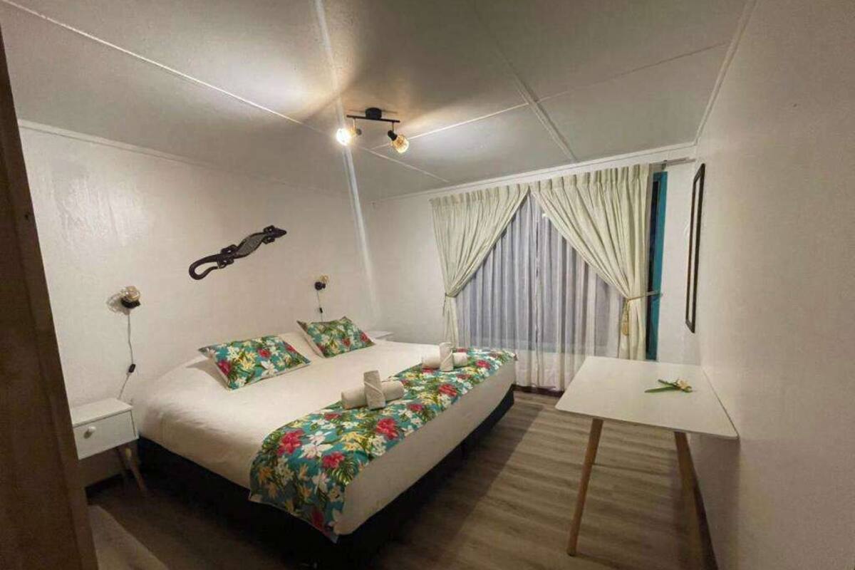 A bedroom with a bed, bedside tables, a desk, curtains, and a ceiling light fixture.