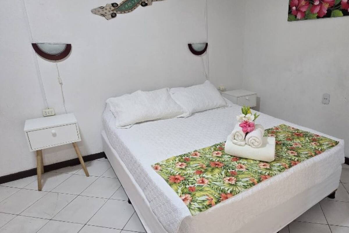 A neatly made bed with a floral bedspread, a small bedside table, and a wall-mounted nightstand.