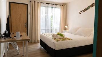 Een hotelkamer met een bed, een bureau, een computer en een raam met gordijnen.