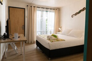 A hotel room with a bed, a desk, a computer, and a window with curtains.