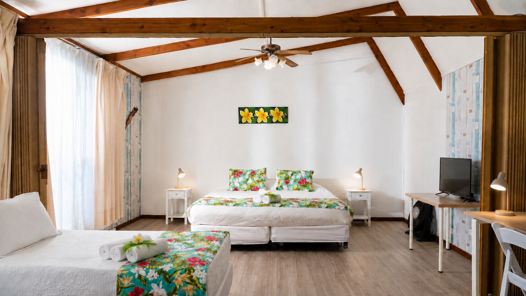 A bedroom with a bed, a desk, a television, and a ceiling fan.