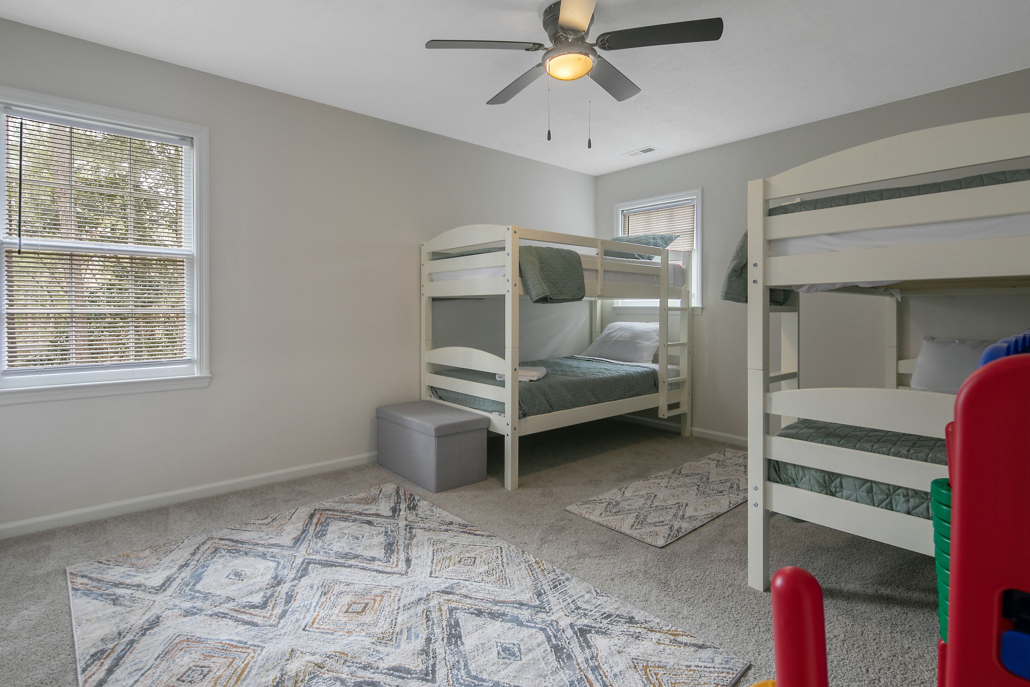 A room with bunk beds, a ceiling fan, and a window with blinds.