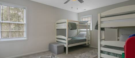 A room with bunk beds, a ceiling fan, and a window with blinds.