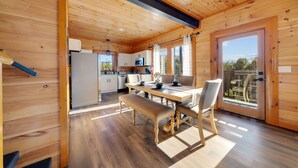 A wooden cabin interior with a dining table, chairs, a bench, a kitchen area, and a sliding glass door to the outside. - Indoor Pool Cabin w/ Theater - Near Douglas Lake (Sevierville)