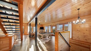 Un intérieur de chalet en bois spacieux, comprenant une table de billard, un ventilateur de plafond et un escalier.