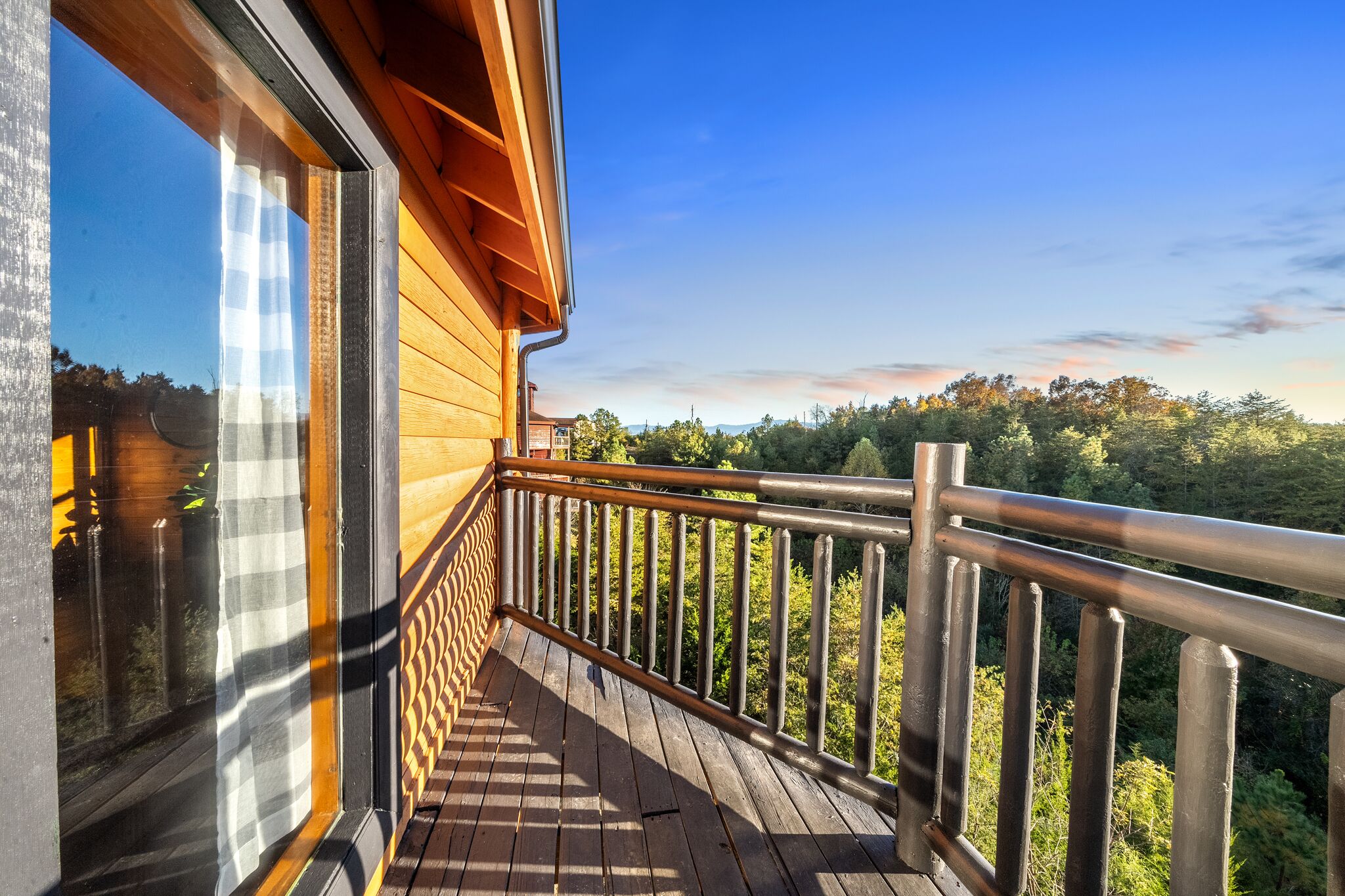 A wooden balcony with a metal railing overlooking a forested area.
