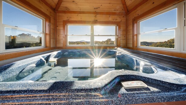 A wooden cabin with a hot tub and large windows offering a view of the landscape. - Indoor Pool Cabin w/ Theater - Near Douglas Lake (Sevierville)