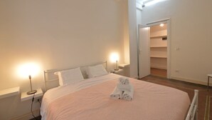 Ein ordentlich gemachtes Bett mit weißen Leinen und einer rosa Decke, eine Nachttischlampe und ein gefaltetes Handtuch auf dem Bett.