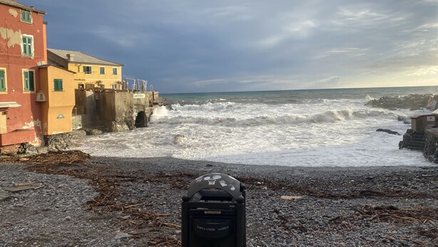 Eine Küstenansicht mit Kiesstrand, einer Seemauer und Gebäuden mit Balkonen.