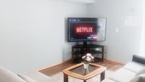 A living room with a flat-screen TV displaying Netflix, a wooden coffee table with a vase, and a grey sofa. - Cozy 2-Bedroom Basement Suite Retreat Calgary (Calgary)