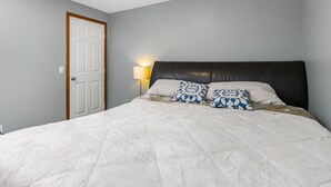 A bedroom with a large bed, a wooden door, and a bedside lamp. - Cozy 2-Bedroom Basement Suite Retreat Calgary (Calgary)