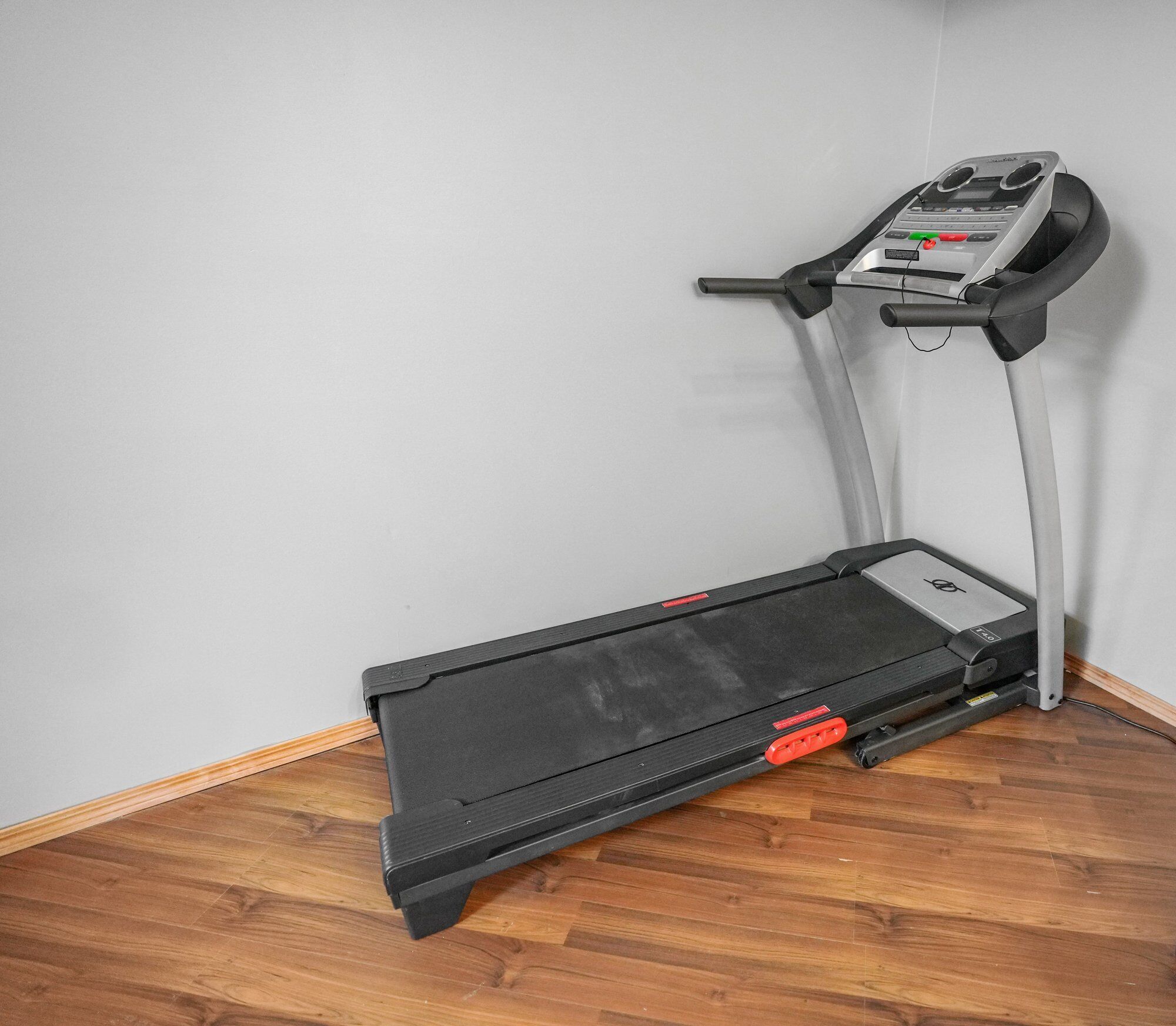 Una cinta de correr en una habitación con suelo de madera y una pared lisa.
