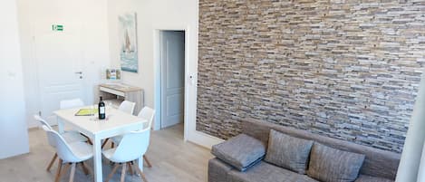 A modern living room with a stone wall, a white dining table with chairs, and a brown sofa with cushions.