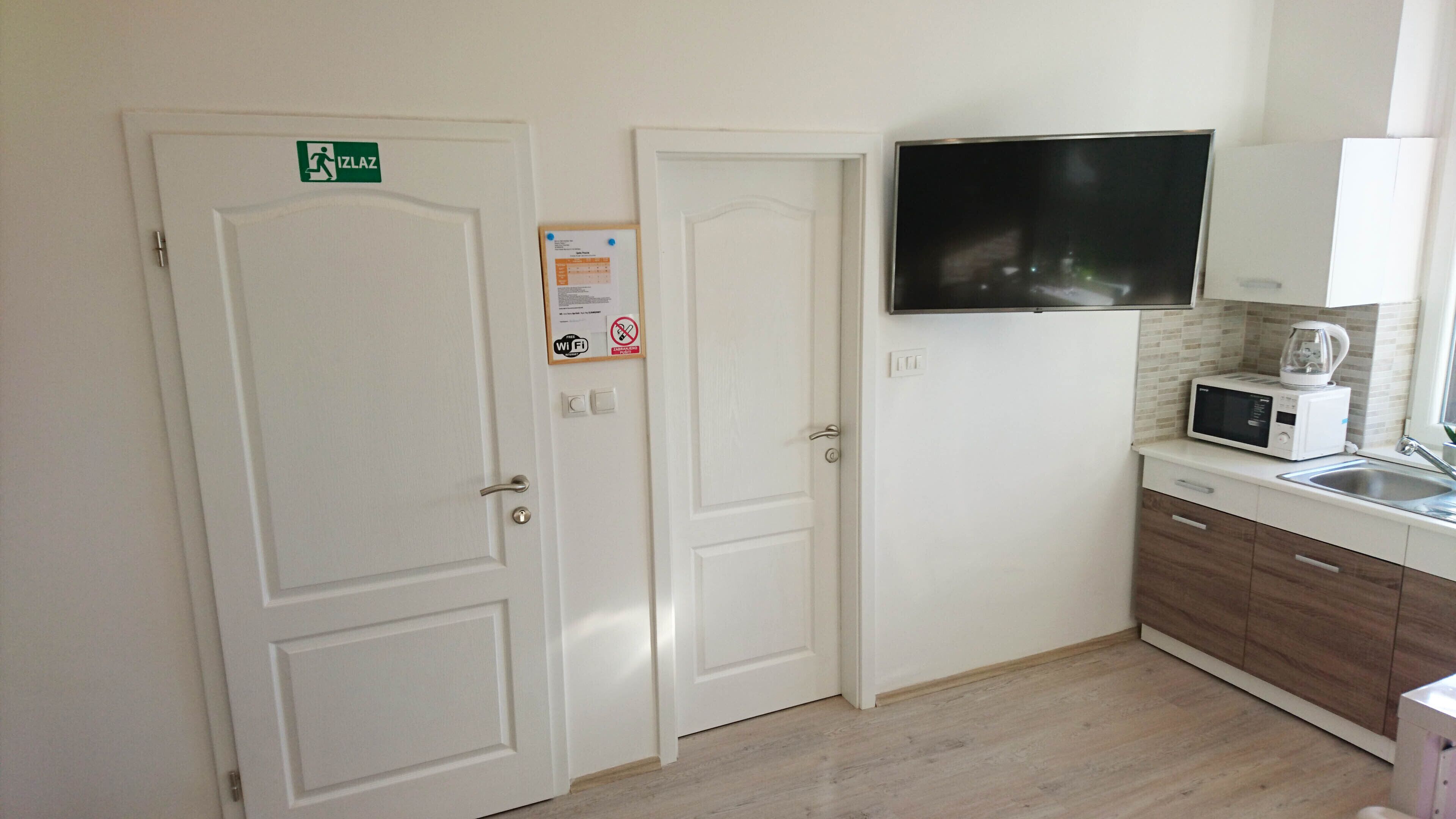 Une cuisine avec des portes blanches, un téléviseur fixé au mur, un four à micro-ondes et une machine à café posée sur le plan de travail.