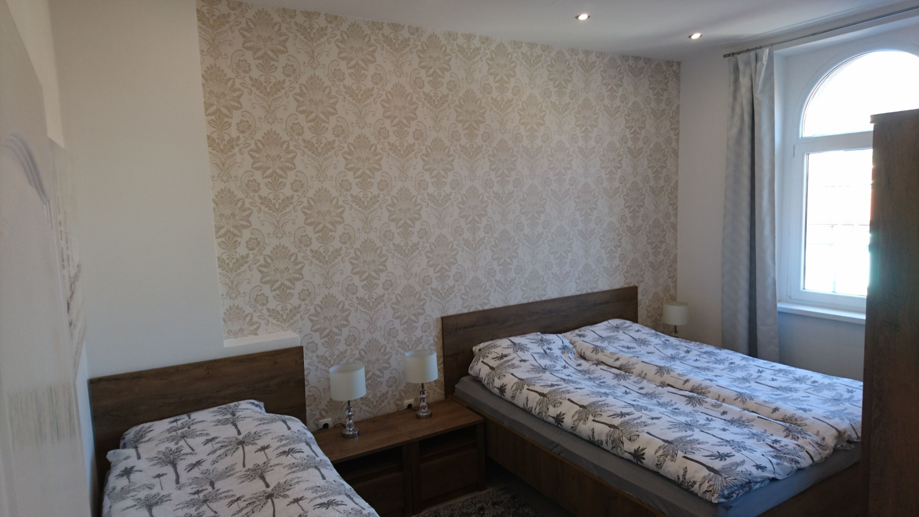 Un dormitorio con dos camas individuales, una mesita de noche con lámpara y una ventana con cortinas.
