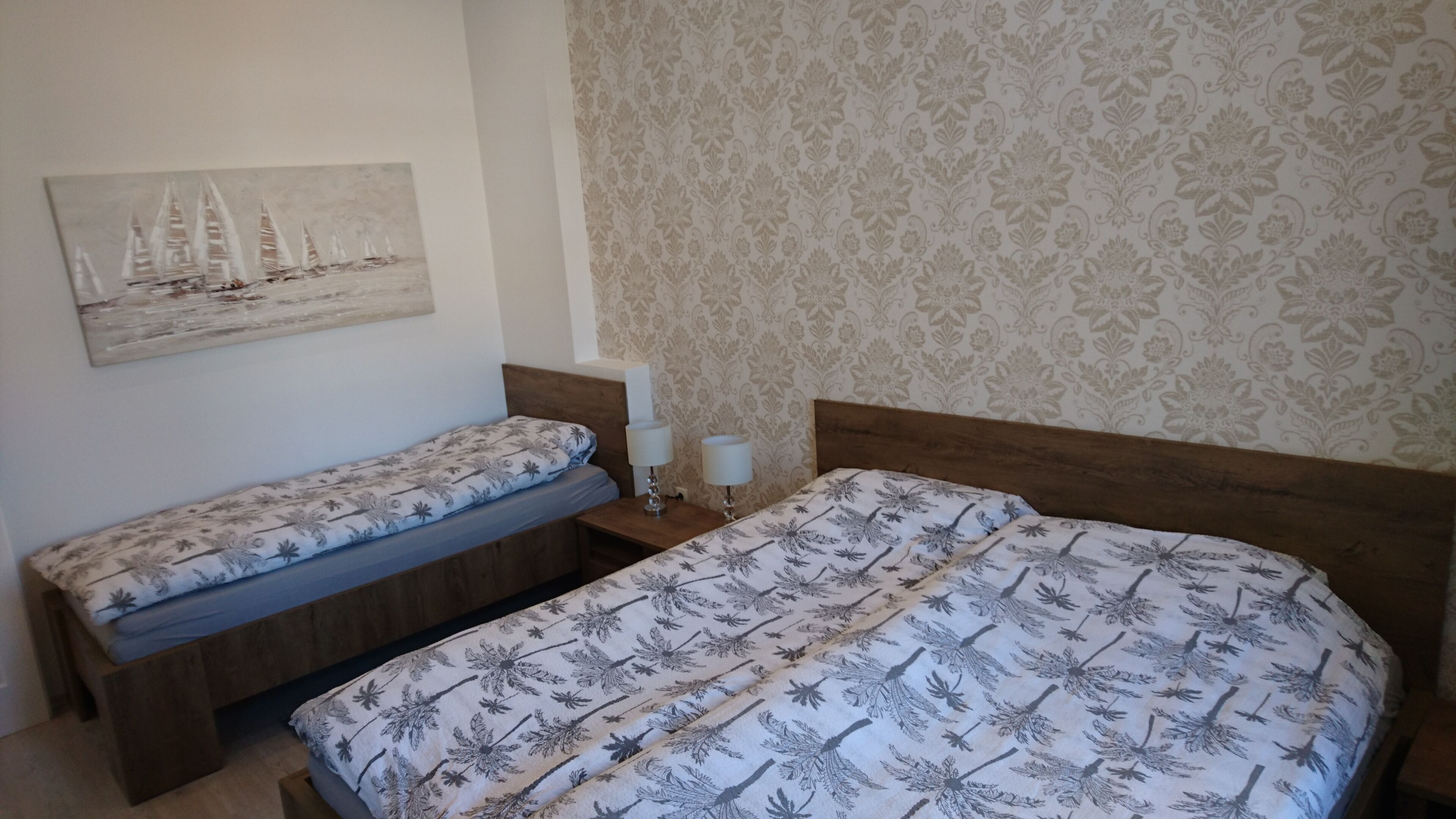 Een slaapkamer met twee bedden, een nachtkastje, een lamp en een schilderij aan de muur.