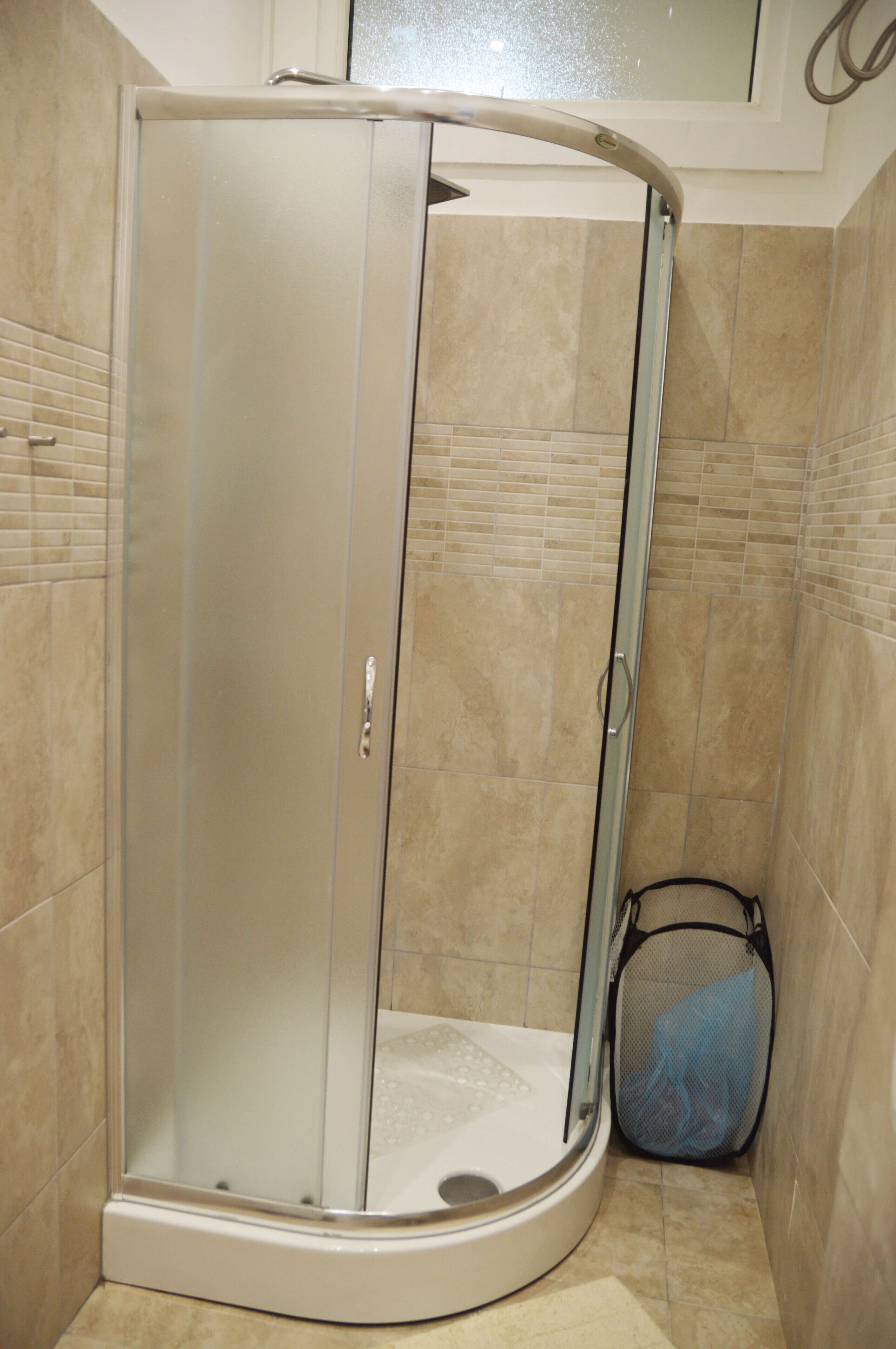 A corner shower enclosure with a glass door, a shower seat, and a handheld showerhead.