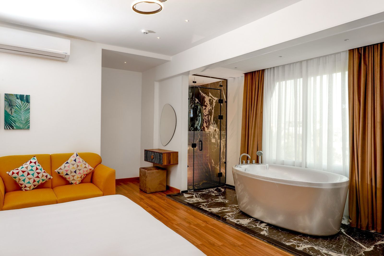 Ett modernt hotellrum med en stor säng, en soffa med mönstrade kuddar, ett badkar och en duschhörna.