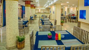 Un vaste espace dédié à la salle à manger, avec plusieurs tables et chaises, agrémenté d’une plante décorative centrale et d’une petite fontaine.