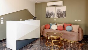 Un espace d’accueil moderne avec un bureau blanc, un canapé agrémenté de coussins colorés et une table basse en verre.