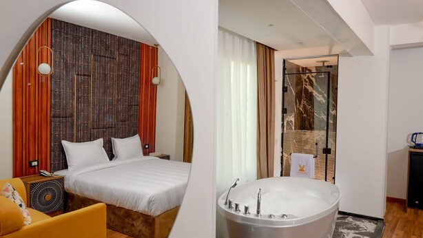 Une chambre d’hôtel avec un lit, un fauteuil jaune, une grande fenêtre et une salle de bain avec une baignoire.