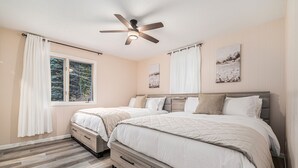 Une chambre avec deux lits, un ventilateur de plafond et une fenêtre avec des rideaux.