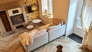 Una sala de estar acogedora con chimenea de piedra, un sofá y un televisor montado en la pared.