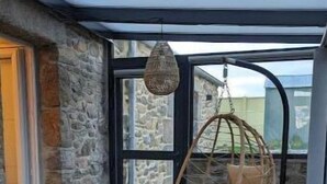 Un interior acogedor con una pared de piedra, una mesa de madera, un sillón colgante y un banco.